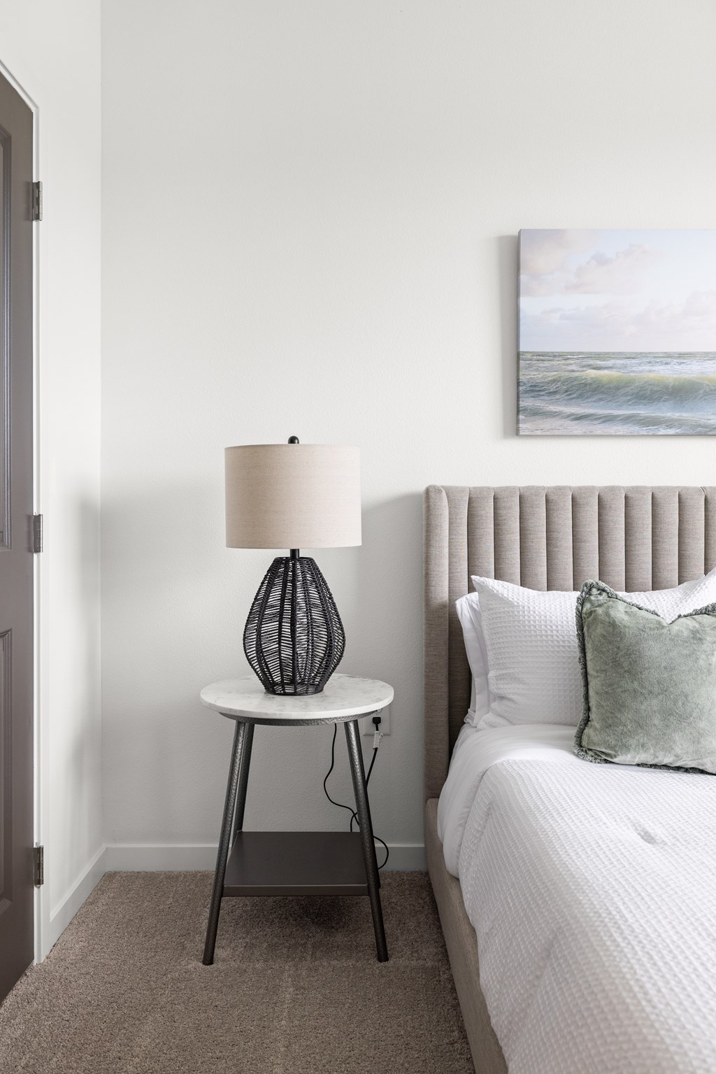 A bedroom with a bed, a side table with a lamp, and a painting on the wall.