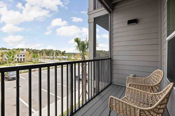 Two chairs are on a balcony with a view of a parking lot and trees.