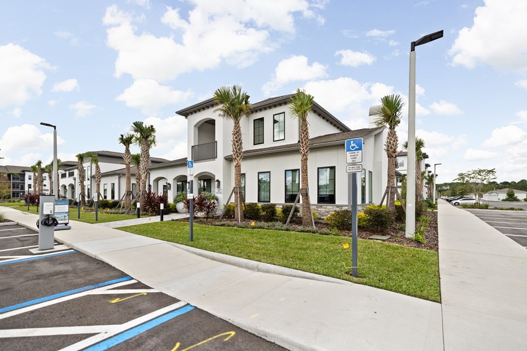 A parking lot with a white building and palm trees in front.