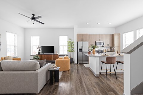 A modern living room with a grey couch, a black television, and a kitchen area in the background.