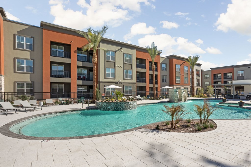 A swimming pool surrounded by palm trees and lounge chairs in front of apartment buildings. at The Maddox Luxury Apartments, Buckeye, AZ, 85326
