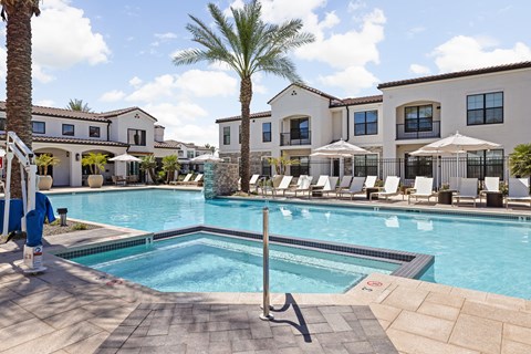 A pool surrounded by lounge chairs and umbrellas with a building in the background.