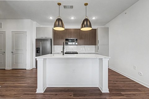 A kitchen with a white island and brown pendant lights.