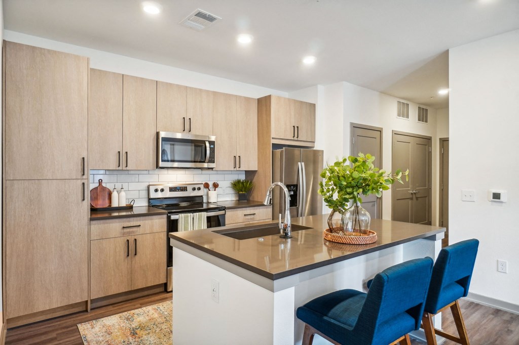 a kitchen with wooden cabinets and a island with blue chairs at Premier at West Park Luxury Apartment Homes, Greeley, CO, 80634