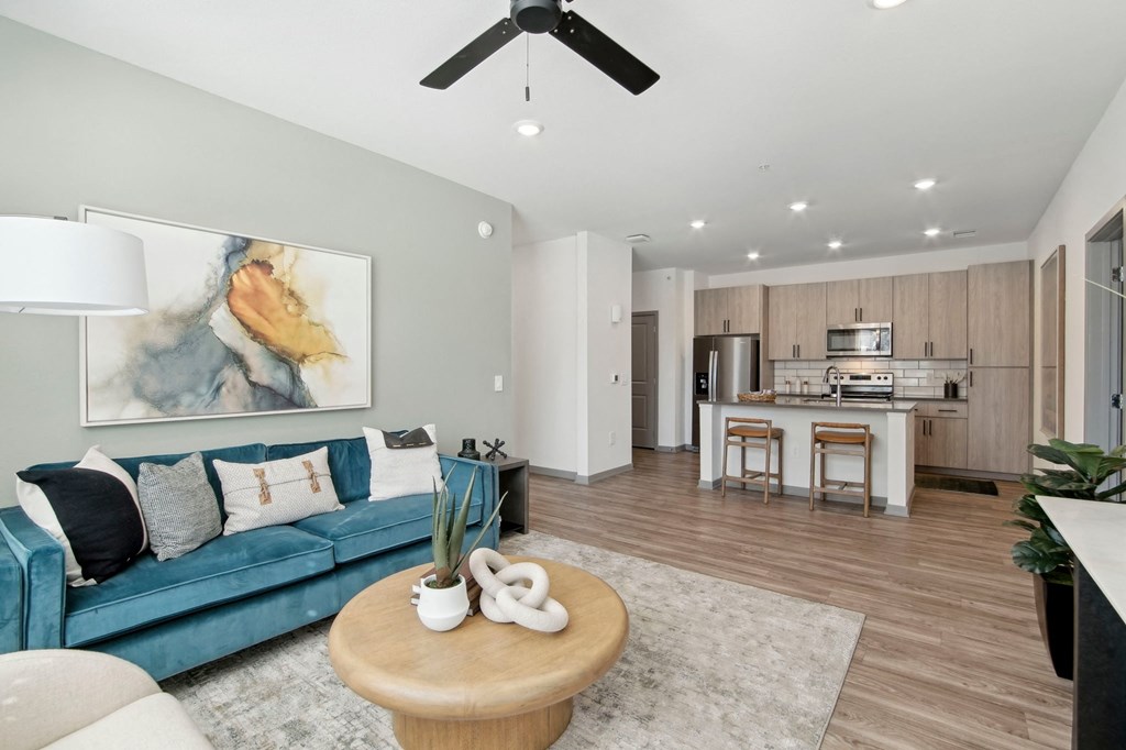 a living room with a blue couch and a kitchen in the background at The Maddox Luxury Apartment Homes, Buckeye