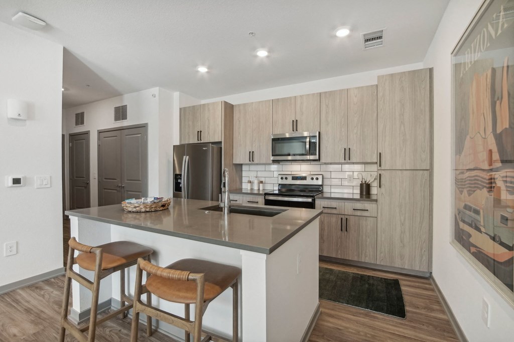 a kitchen with a large island with two stools in front of a counter top at The Maddox Luxury Apartment Homes, Buckeye, 85326