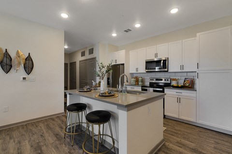 a kitchen with white cabinets and a large island with two stools  at Upland Flats, Colorado Springs, CO