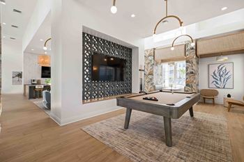 A pool table is in the middle of a room with a television and a chair.