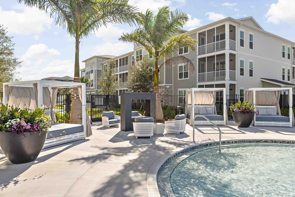 A pool area with a hot tub and lounge chairs in front of a multi-story apartment building.
