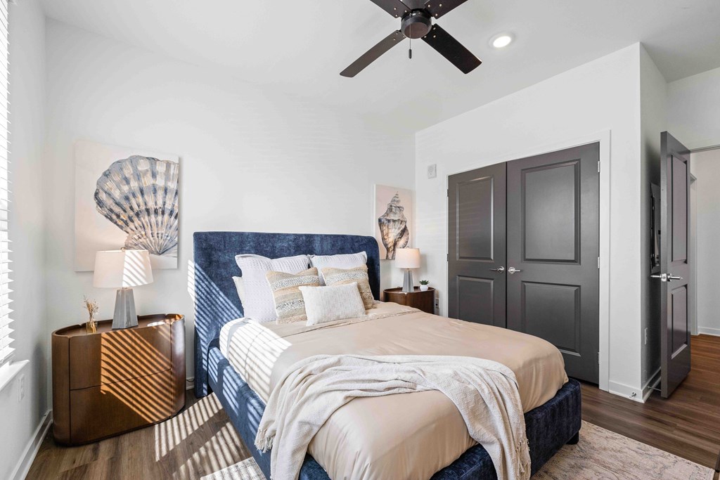A bedroom with a bed, a ceiling fan, and a wooden nightstand.