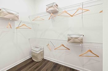 A white closet with orange hangers and a trash can.