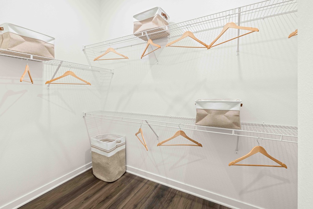 A white closet with orange hangers and a trash can.