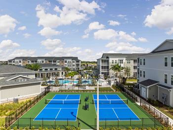 A tennis court is surrounded by a fence and apartment buildings.