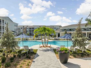 A pool surrounded by trees and chairs with a building in the background.