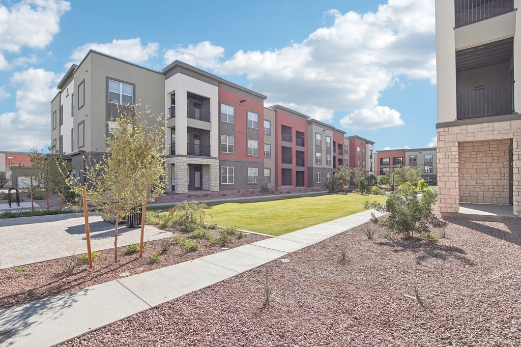 an exterior view of a row of apartment buildings with a lawn and sidewalk at The Maddox Luxury Apartment Homes, Buckeye, AZ