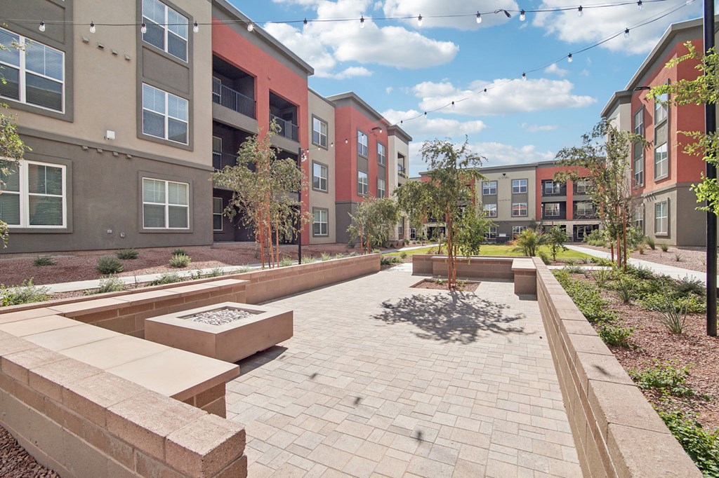 an outdoor area with benches and trees in front of an apartment building at The Maddox Luxury Apartment Homes, Buckeye, AZ 85326