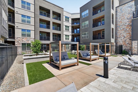 A modern outdoor seating area with a wooden swing set and a stone wall.