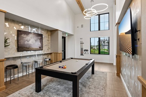 A pool table is in the middle of a room with a bar and a television.