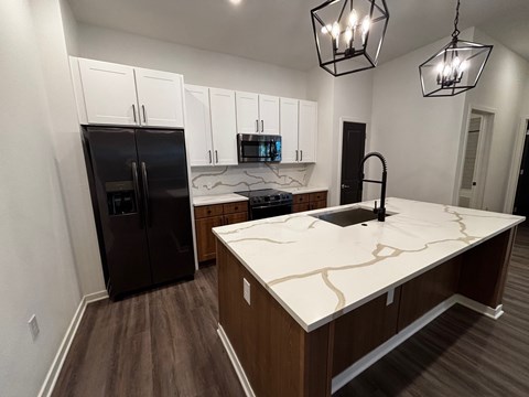 A kitchen with a black refrigerator and a marble countertop.