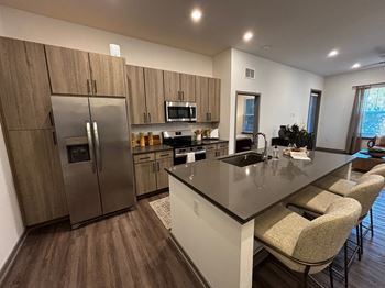 A modern kitchen with a refrigerator, microwave, oven, sink, and bar stools. at The Concord Luxury Apartments, Sarasota, FL