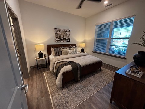 A bedroom with a large bed, a nightstand with a lamp, and a painting on the wall.