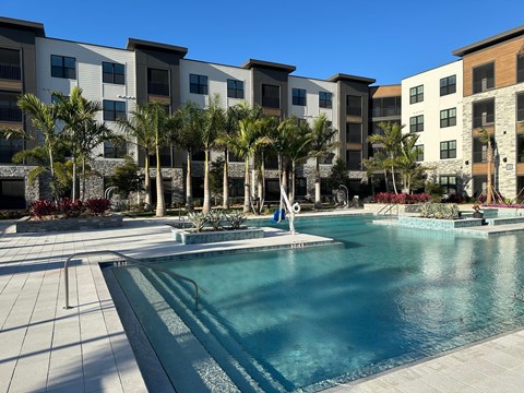 A swimming pool in front of apartment buildings with palm trees.
