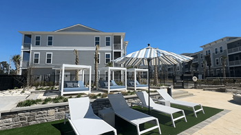 A white striped umbrella is in the middle of a patio with white chairs at The Quinn Luxury Apartments, Pensacola 32526