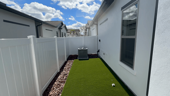 A white fence separates a small grassy area from a white house.