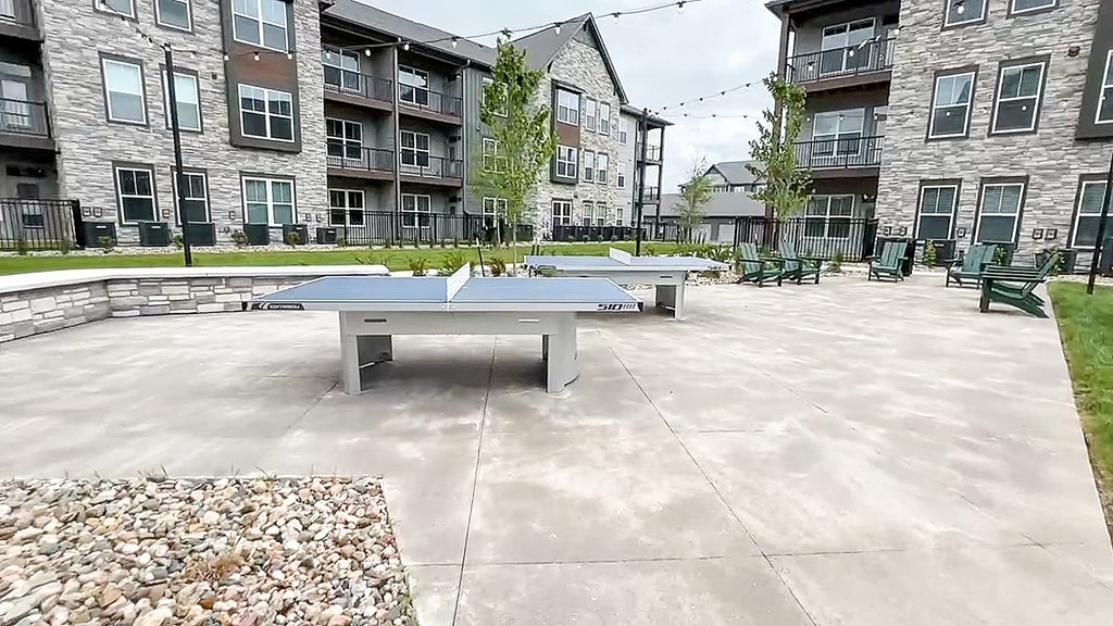 two ping pong tables in a courtyard with an apartment building at The Depot, Missouri, 64083