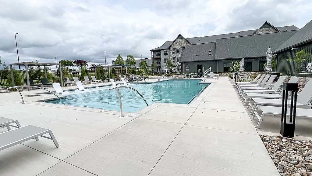 a swimming pool with white chairs next to a building at The Depot, Raymore, MO