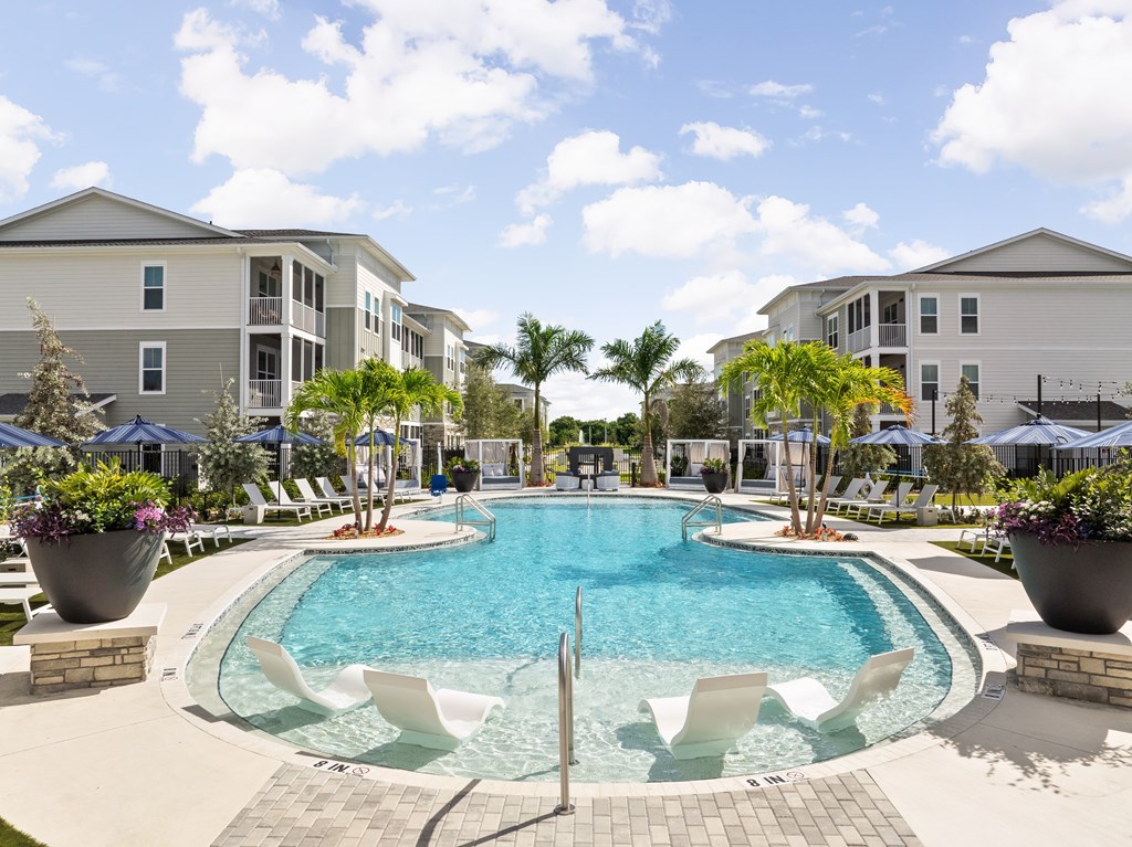 A swimming pool surrounded by white chairs and potted plants.