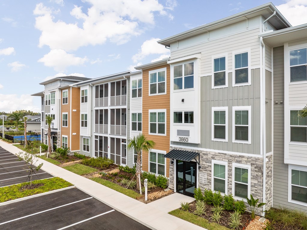 A row of modern apartment buildings with a parking lot in front.