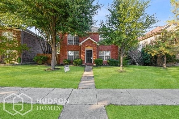 the front of a brick house with a lawn and trees