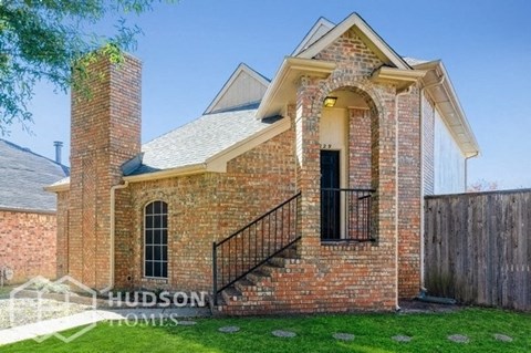 the front of a brick house with a balcony and a yard