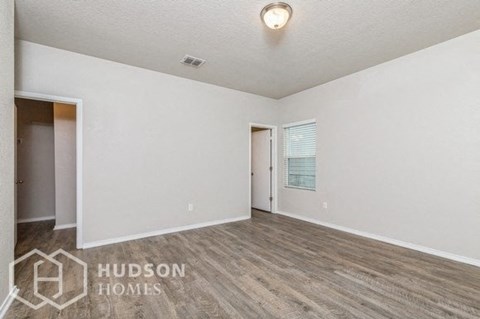 A spacious room with wooden flooring and white walls, branded with "HUDSON HOMES".
