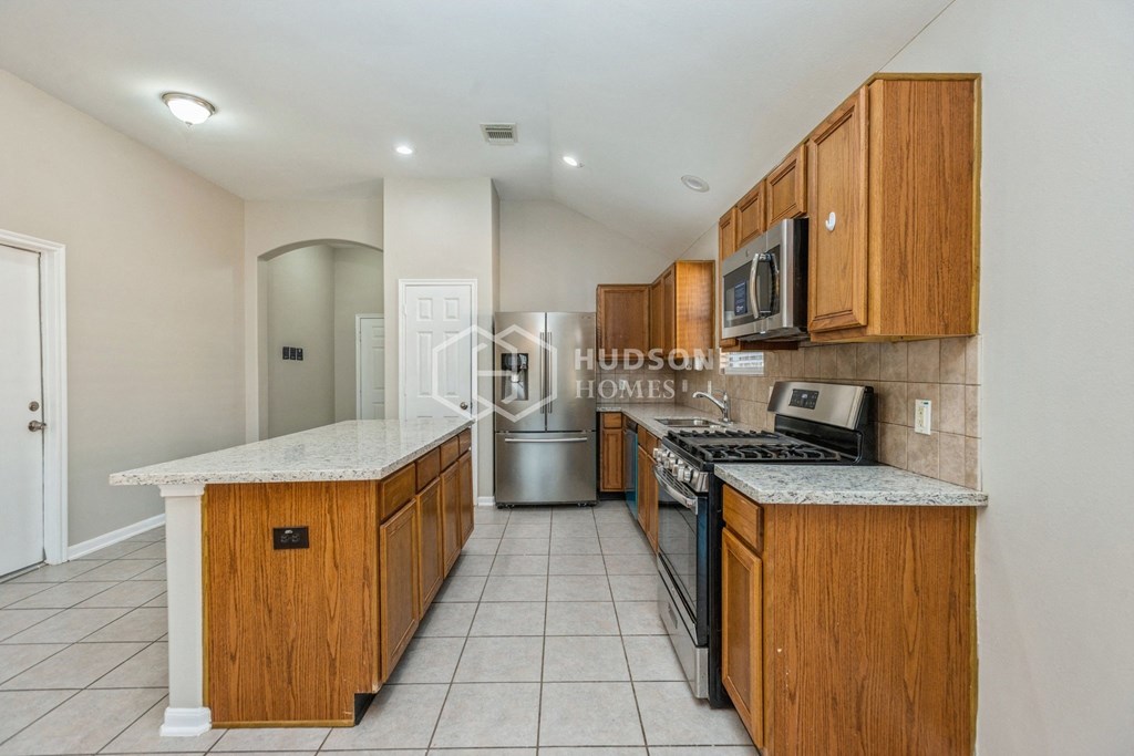 a kitchen with wood cabinets and white countertops and a stainless steel stove and refrigerator