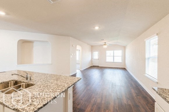 an empty kitchen and living room with wood flooring and granite counter tops