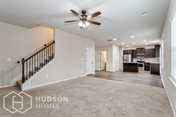 an empty living room with a ceiling fan and a staircase