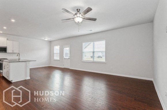 an empty living room with a kitchen and a ceiling fan