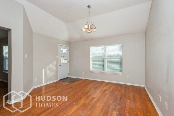 an empty living room with wood flooring and a door to the kitchen