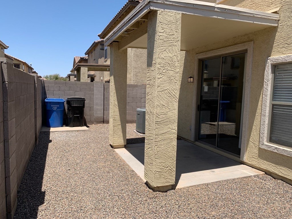 a patio outside of a house with a backdoor and a trash can