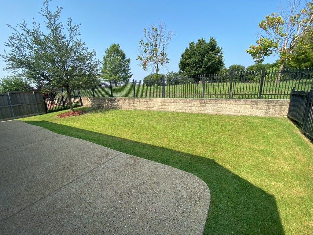 a yard with a sidewalk and a black fence