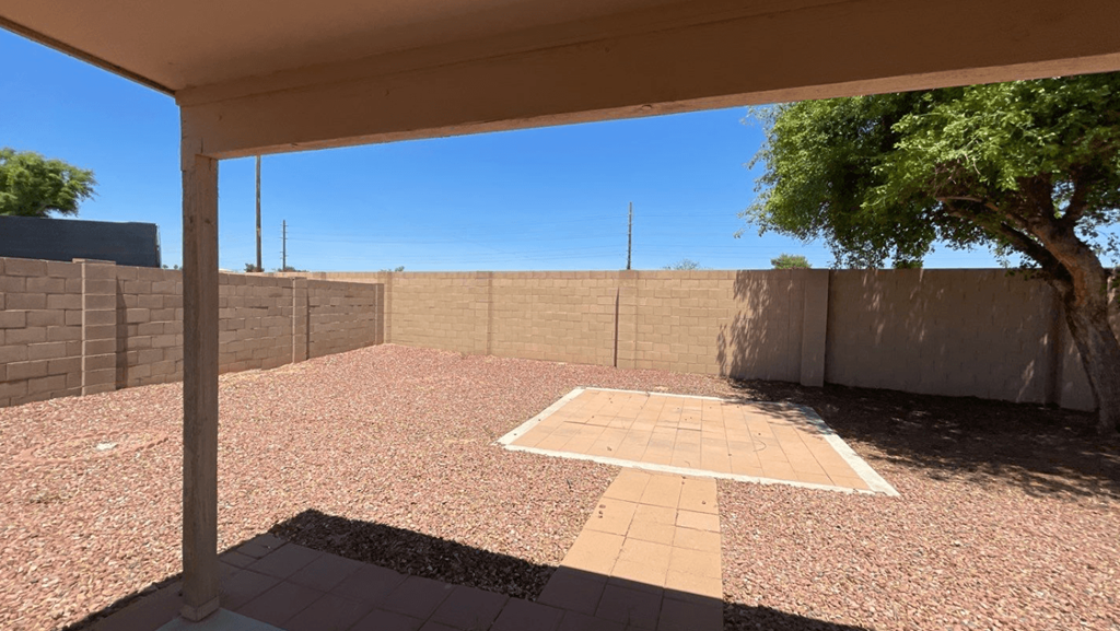 an empty yard with a tree and a brick wall