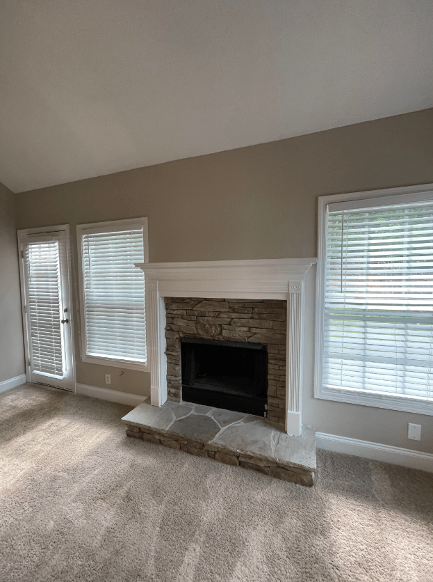 a living room with a stone fireplace and two windows