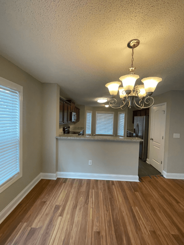 an empty living room with a kitchen and a chandelier