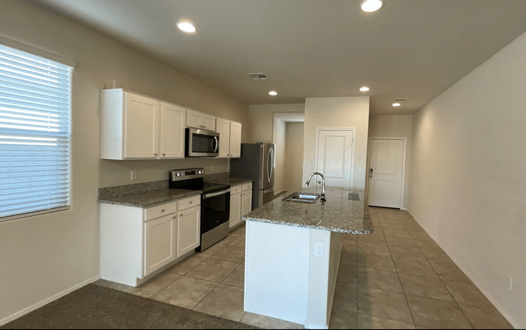 an empty kitchen with white cabinets and a granite counter top