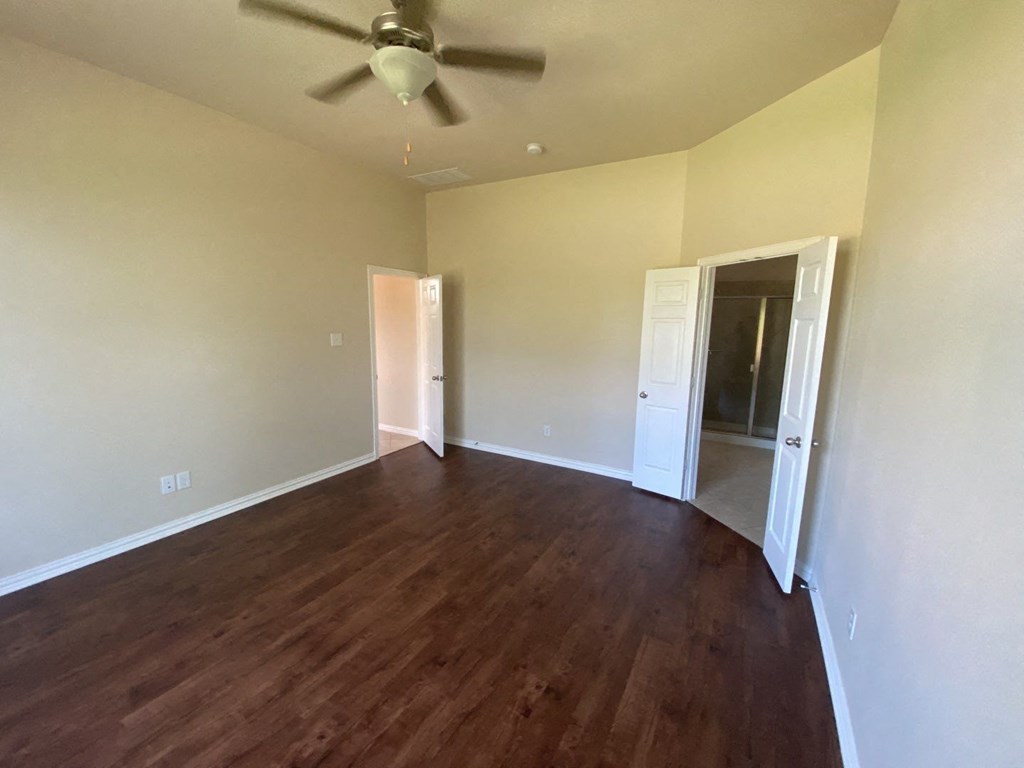an empty living room with wood floors and a ceiling fan