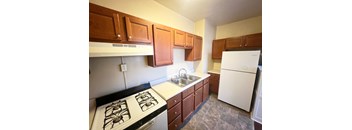 A kitchen with white appliances and brown cabinets.at North Pointe Commons Apts, Pittsburgh, PA