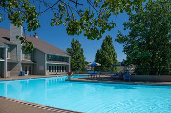 A swimming pool in front of a building with trees around at Belmont Ridge Apartments, Monroeville, PA, 15146
