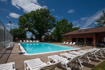 A pool surrounded by white chairs and trees at Deauville Park Apartments, Monroeville, PA
